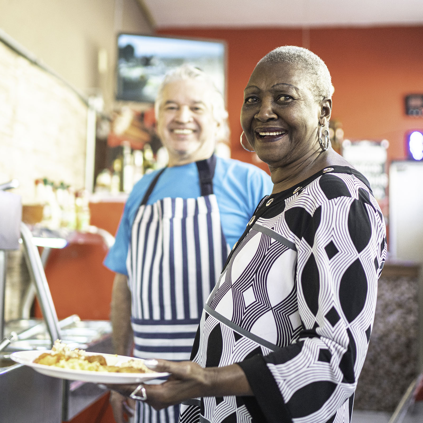 Portrait of senior waiter helping customer to choose food at self service restaurant